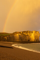 Golden sunset over the cliffs of Étretat, Normandy, France, with a rainbow above the sea. Dramatic coastal landscape showcasing natural beauty and serene atmosphere.