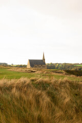 Small chapel on the cliff at Étretat, Normandy, France, surrounded by green hills and cloudy sky. Peaceful coastal landscape with natural and architectural harmony.