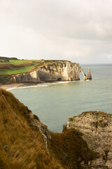 Famous white cliffs of Étretat, Normandy, France, rising above turquoise sea waters. Iconic coastal landscape known for its natural beauty and dramatic rock formations.