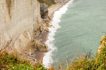 Famous white cliffs of Étretat, Normandy, France, rising above turquoise sea waters. Iconic coastal landscape known for its natural beauty and dramatic rock formations.