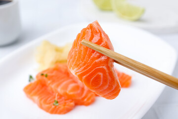 Chopsticks with fresh salmon sashimi against blurred background, closeup