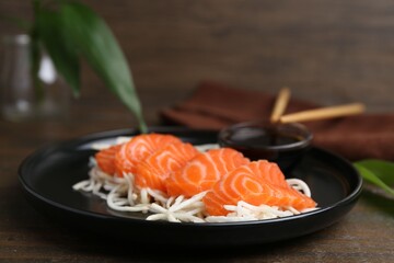 Fresh salmon sashimi with sliced radish and soy sauce on wooden table, closeup