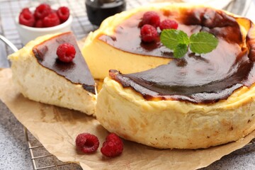 Tasty Basque cheesecake with raspberries and mint on light grey textured table, closeup