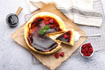 Tasty Basque cheesecake with raspberries, mint and chocolate topping on light grey textured table, flat lay