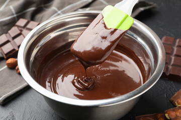 Melted chocolate and pieces with hazelnuts on black table, closeup