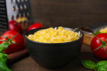 Grated cheese, grater, tomatoes and basil on wooden table, closeup