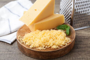 Grated and pieces of cheese with grater and basil on wooden table, closeup