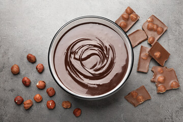 Melted chocolate in bowl, pieces and nuts on grey table, flat lay