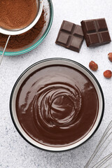 Melted chocolate in bowl, pieces, nuts, cocoa powder and whisk on light grey table, flat lay