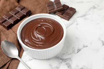 Melted chocolate in bowl, pieces and spoon on white marble table, closeup. Space for text