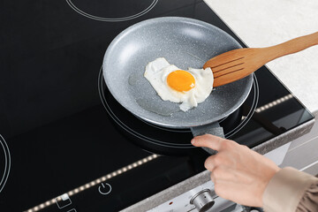 Woman taking fried egg with slotted spatula in kitchen, closeup