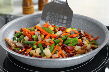 Stirring mix of fresh vegetables with slotted spatula in frying pan, closeup