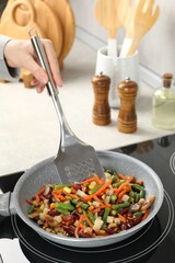Woman stirring mix of fresh vegetables with slotted spatula in frying pan, closeup