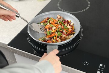 Woman stirring mix of fresh vegetables with slotted spatula in frying pan, closeup