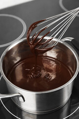 Whisk with melted chocolate above pot, closeup