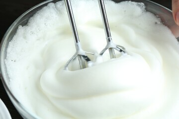 Woman whisking egg whites with hand mixer at table, closeup