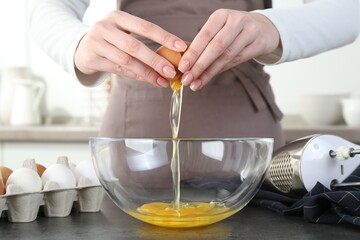 Woman cracking egg into bowl at grey table in kitchen, closeup