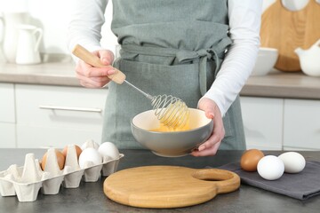 Woman beating eggs with whisk at grey table in kitchen, closeup