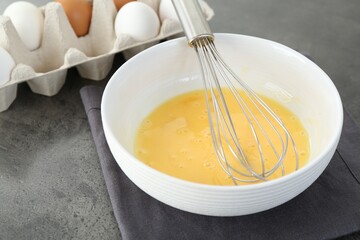 Broken eggs in bowl with whisk on grey table, closeup