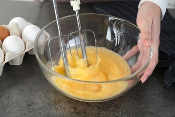 Woman beating eggs with mixer at grey table, closeup