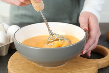 Woman beating eggs with whisk at grey table in kitchen, closeup