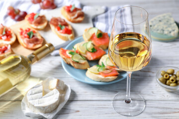 Tasty bruschettas with salmon, cucumber, prosciutto and wine on white wooden table, selective focus