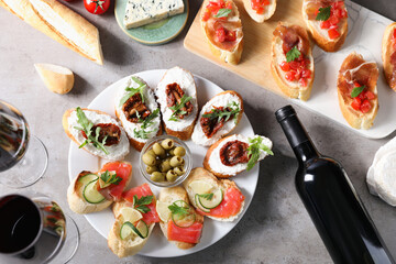 Different tasty bruschettas and red wine on grey textured table, flat lay