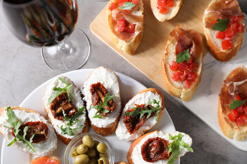 Different tasty bruschettas and red wine on grey textured table, flat lay