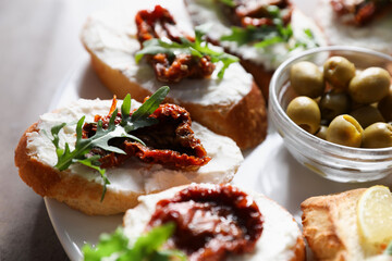 Tasty bruschettas with cream cheese, sun dried tomatoes, arugula and olives on grey table, closeup