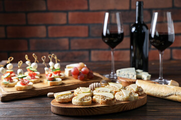 Different tasty bruschettas and red wine on wooden table against brick wall, closeup