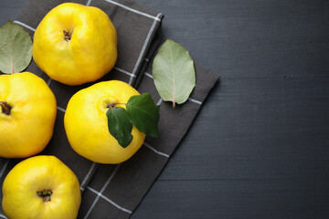 Ripe quinces and green leaves on black wooden table, top view. Space for text