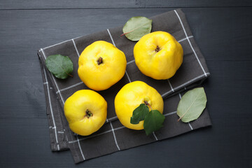 Ripe quinces and green leaves on black wooden table, top view