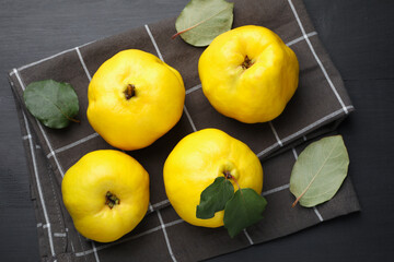 Ripe quinces and green leaves on black wooden table, top view