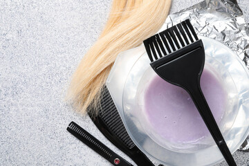 Hair dyeing product in bowl, lock of hair and different hairdresser's tools on light grey table, flat lay. Space for text