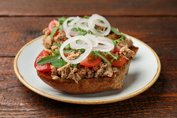 Delicious bruschettas with tuna, tomatoes, onion and arugula on wooden table, closeup