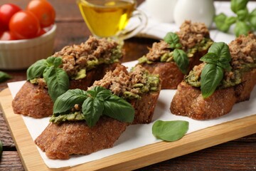Delicious bruschettas with tuna, avocado and basil on wooden table, closeup