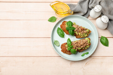Delicious bruschettas with tuna, avocado and basil served on light wooden table, flat lay. Space for text