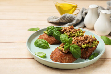 Delicious bruschettas with tuna, avocado and basil served on light wooden table, closeup