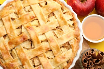 Tasty homemade apple pie and ingredients on yellow background, flat lay