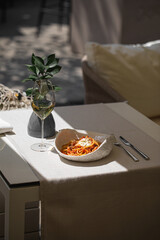 Spaghetti pasta with tomato sauce and cheese served with white wine on sunny elegant table with fork and knife