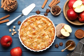 Delicious homemade apple pie in baking dish, ingredients and spatula on blue wooden table, flat lay