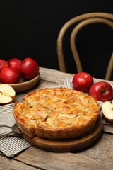 Delicious homemade pie and apples on wooden table against black background
