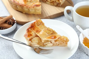 Piece of delicious homemade apple pie, spices and tea on grey textured table, closeup