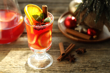 Tasty punch drink in glass, spices and Christmas decor on wooden table, closeup