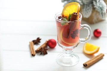 Tasty punch drink in glass, spices and Christmas decor on white wooden table, closeup. Space for text
