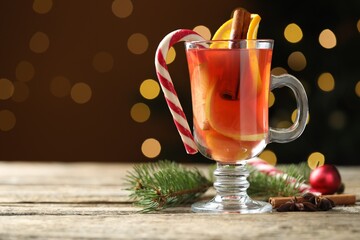 Tasty punch drink in glass, spices and Christmas decor on wooden table against background with blurred lights, space for text. Bokeh effect