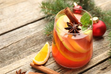 Tasty punch drink in glass, spices and Christmas decor on wooden table, closeup. Space for text