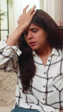 Indian woman at home taps forehead realizing mistake feeling embarrassed deeply and regretful. Arabian girl on sofa makes facepalm gesture showing repentance self blame confusion surprise and anxiety.