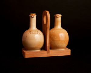 Rustic pottery oil and vinegar cruets in a wooden caddy, against a dark background. Earthy tones, handmade feel for kitchen condiments.