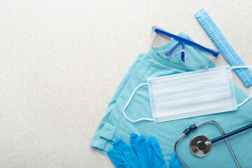 Healthcare background of disposable face mask, gloves, cap, goggles, scrubs and stethoscope laying on table flat lay view